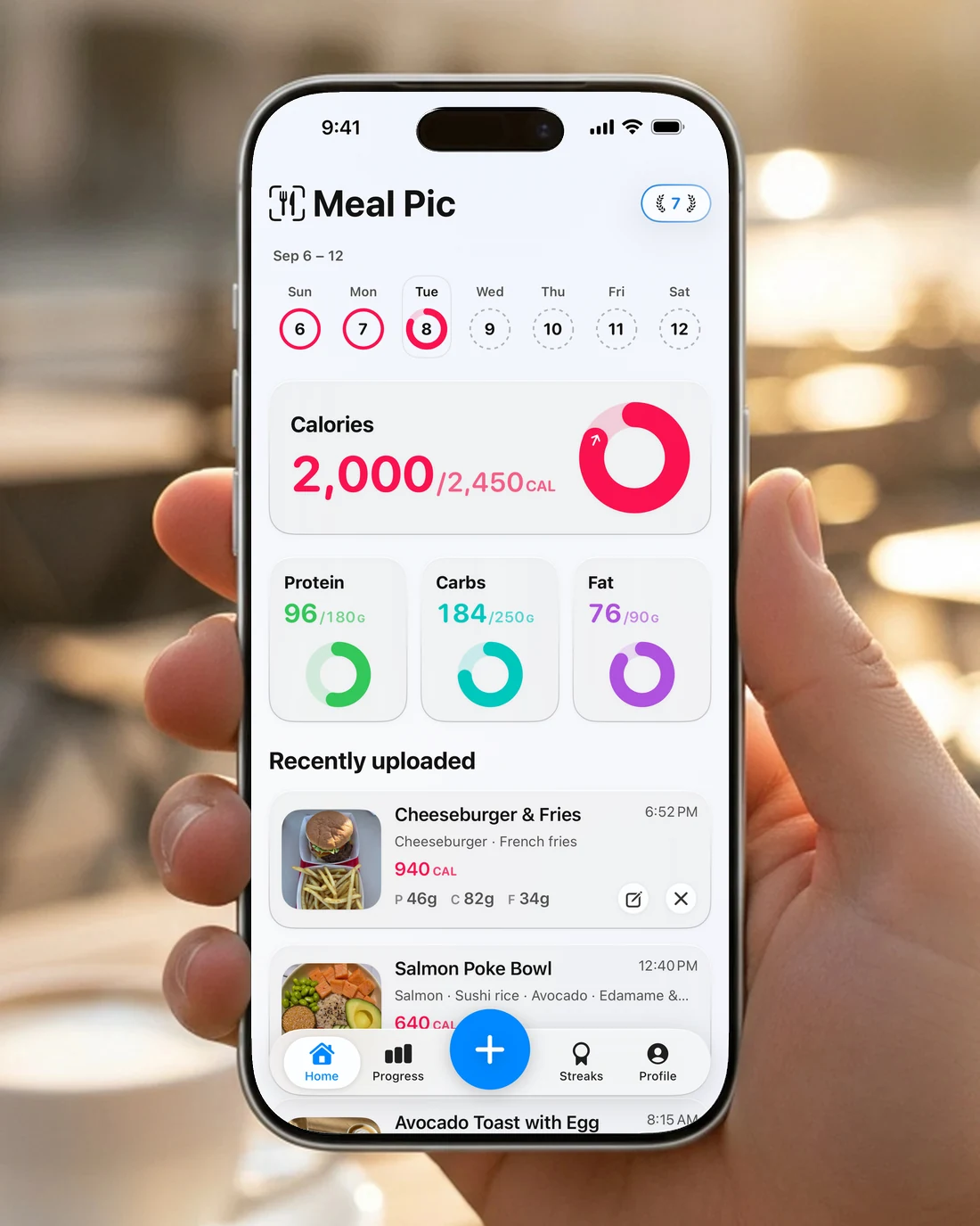 A hand holding an iPhone showing the Meal Pic home screen with calorie and macro rings